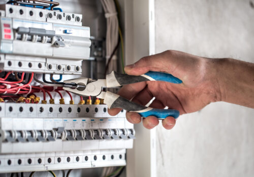 Man, an electrical technician working in a switchboard with fuses. Installation and connection of electrical equipment. Professional with tools in hand. concept of complex work, space for text.